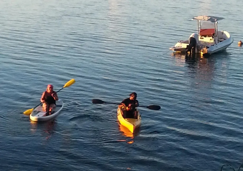 Deux personnes pagayent sur l'eau calme, un bateau est amarré au loin.