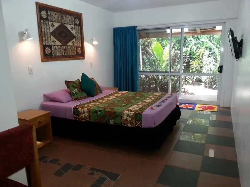 Une chambre lumineuse avec un grand lit recouvert d'une courtepointe colorée et un accès à une terrasse.
