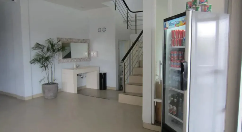 Une piece lumineuse avec un escalier et un refrigerateur rempli de boissons.
