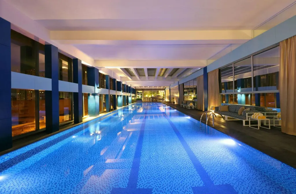 Une longue piscine intérieure illuminée avec des transats sur le côté.