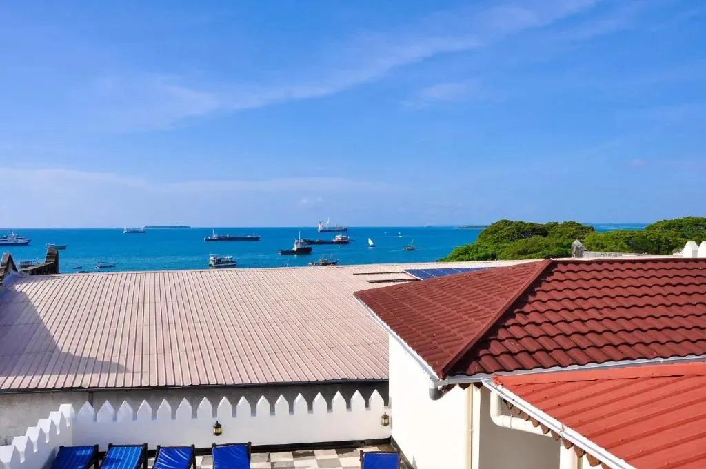 Toits de bâtiments avec vue sur la mer et des bateaux à l'horizon.