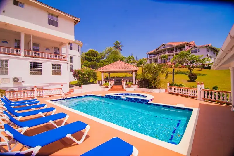 Une piscine rectangulaire bordée de transats bleus, devant un bâtiment blanc à plusieurs étages.