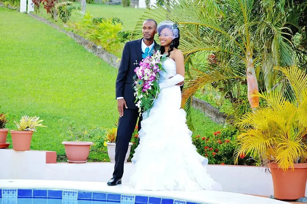 Un couple en tenue de mariage pose près d'une piscine dans un jardin verdoyant.