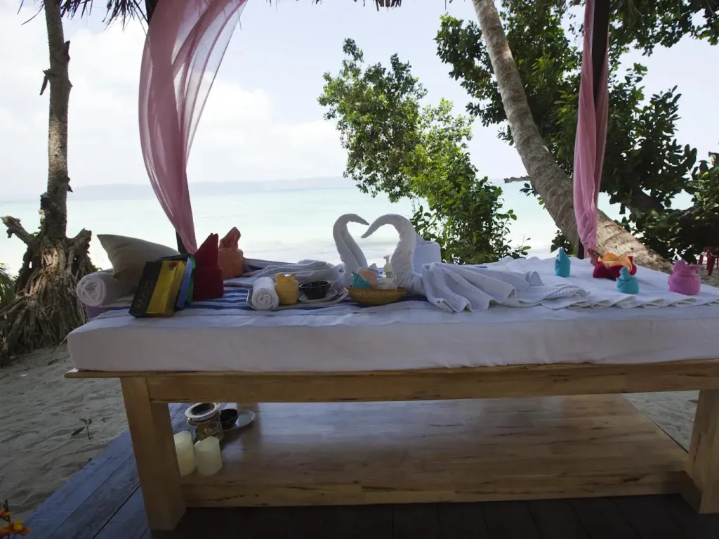 Table de massage en plein air face à la mer, décorée de serviettes et de fleurs.