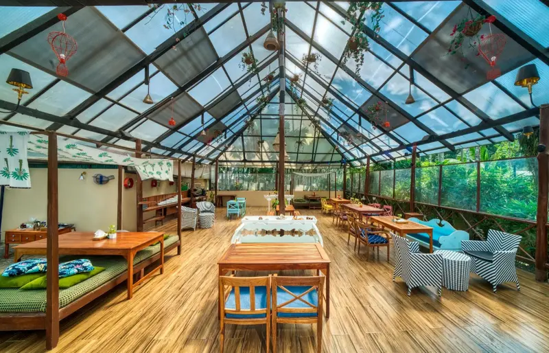 Une salle lumineuse avec des tables et des chaises en bois, sous une toiture vitrée.