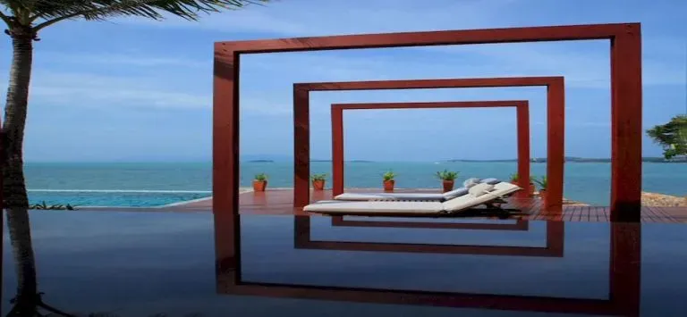Transats blancs alignés au bord d'une piscine à débordement avec vue sur la mer.