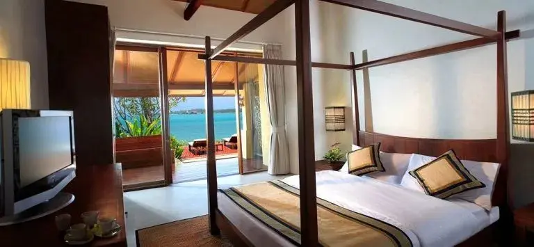 Une chambre lumineuse avec un grand lit à baldaquin donnant sur une terrasse et la mer.