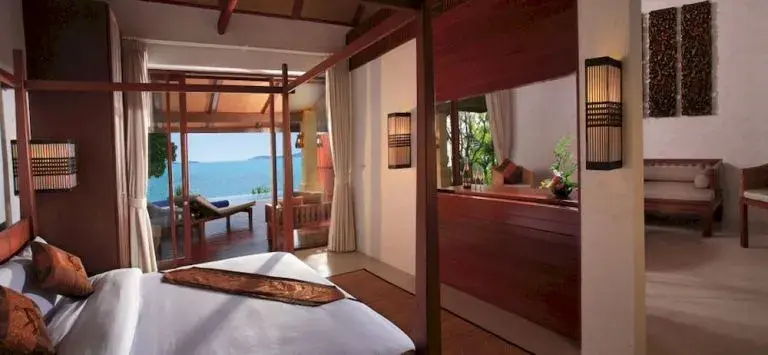 Une chambre lumineuse avec un lit à baldaquin donnant sur une terrasse et la mer.
