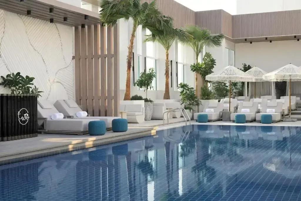 Une piscine rectangulaire bordée de transats blancs et de parasols.