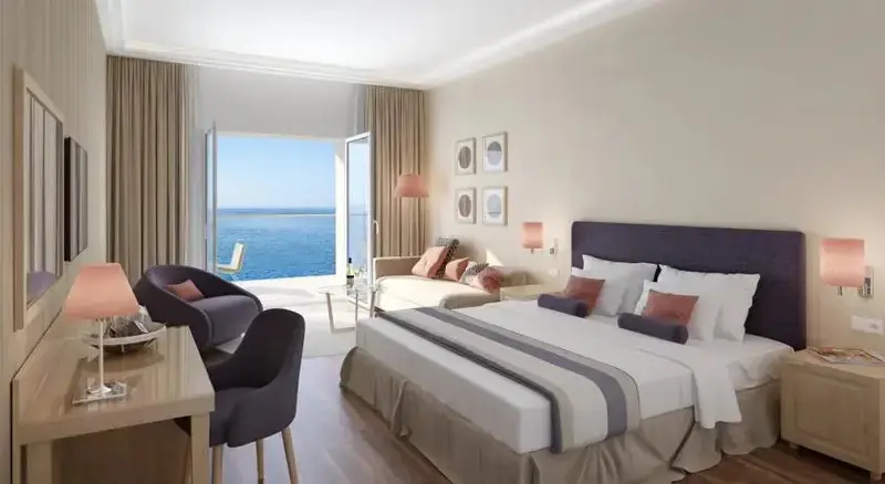 Chambre lumineuse avec un grand lit et vue sur la mer par de larges baies vitrées.
