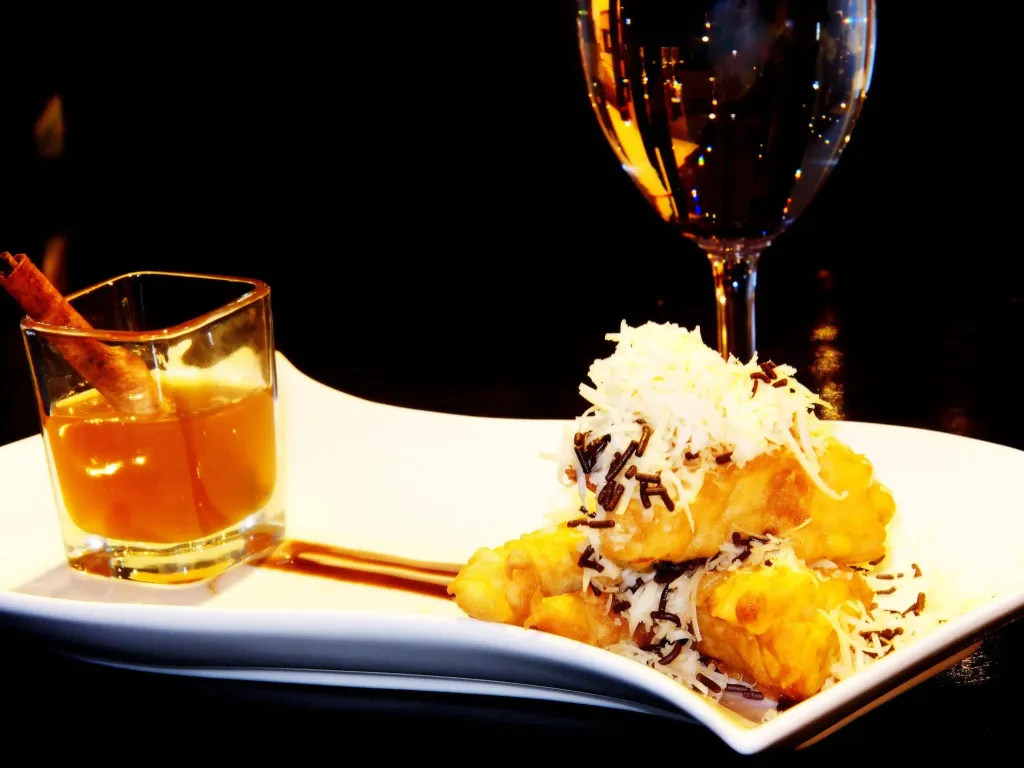 Assiette de beignets recouverts de noix de coco râpée et de copeaux de chocolat, accompagnée d'un verre de boisson ambrée.