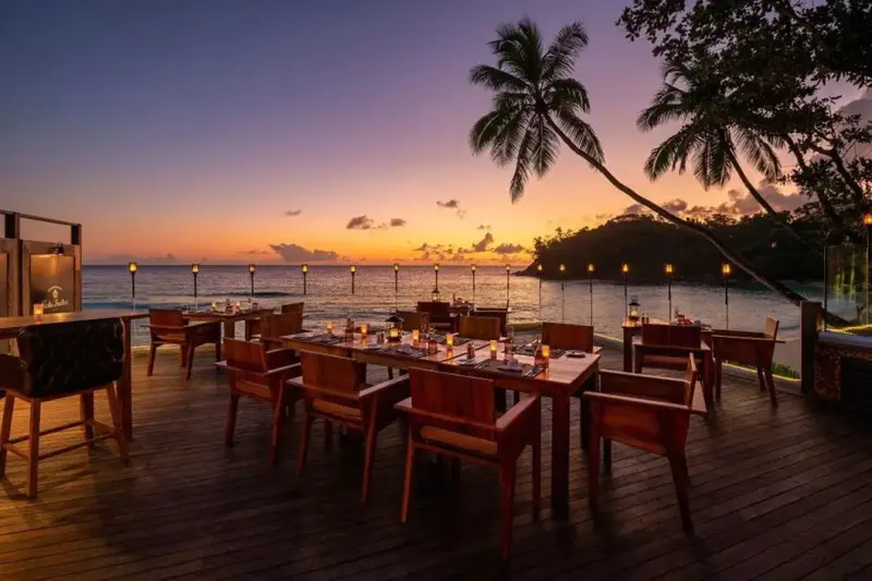 Tables de restaurant en terrasse face à la mer au coucher du soleil.