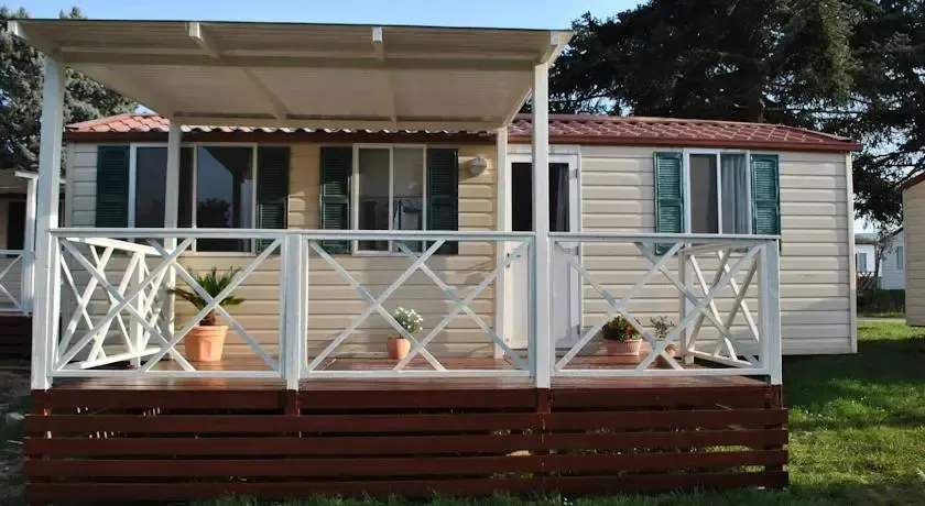 Mobil-home avec terrasse couverte et végétation en pots.