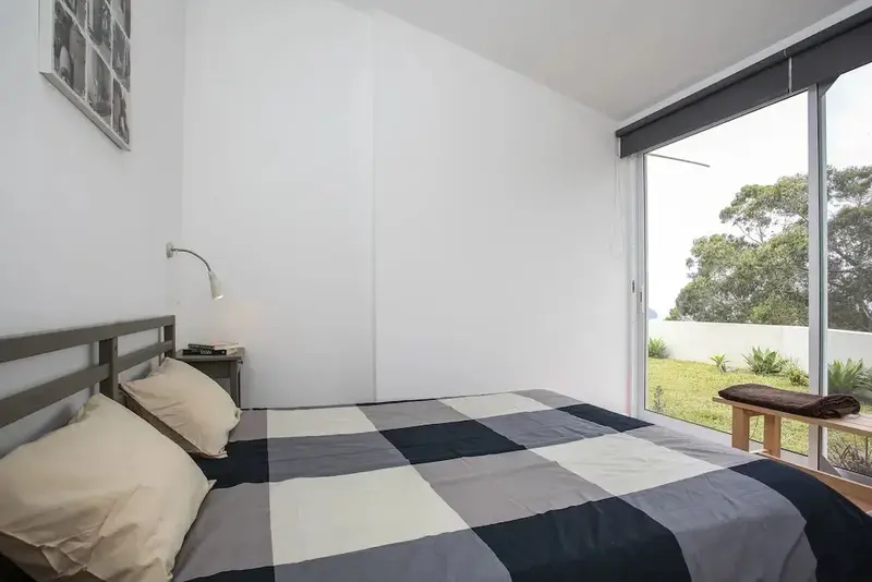 Une chambre lumineuse avec un lit recouvert d'une couverture à carreaux donnant sur un jardin.