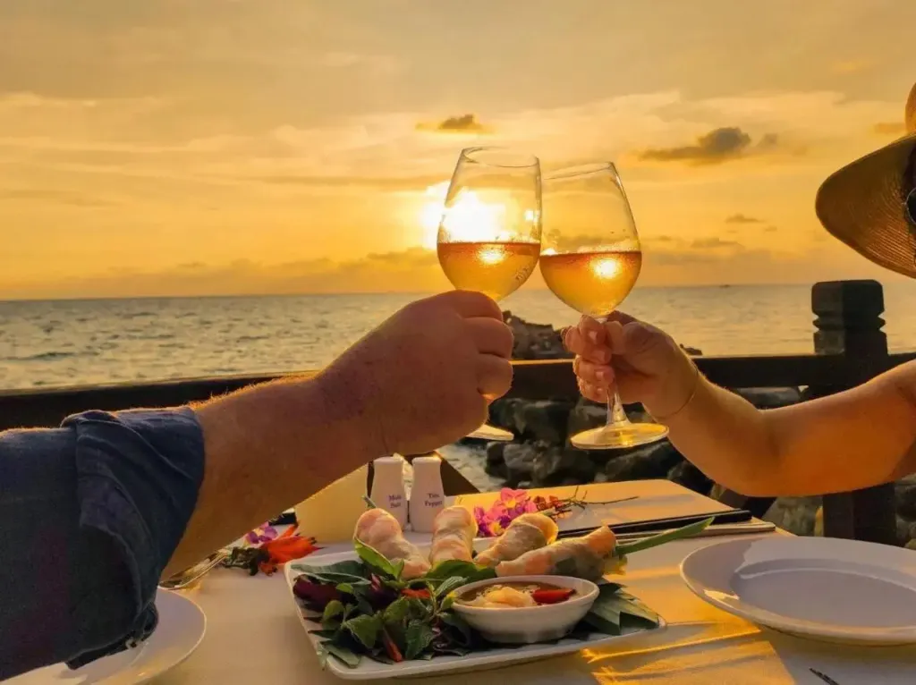 Deux personnes trinquent avec des verres de vin face à un coucher de soleil sur la mer.