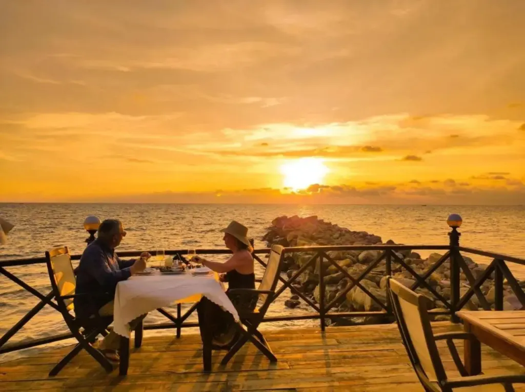 Un couple dîne en terrasse face à la mer au coucher du soleil.