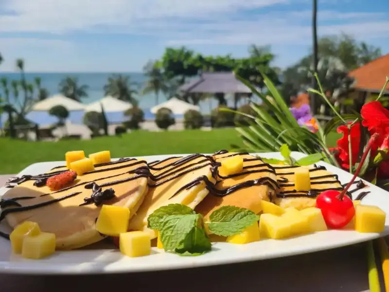 Assiette de crêpes garnies de fruits et de chocolat, avec une vue sur la mer et la plage en arrière-plan.