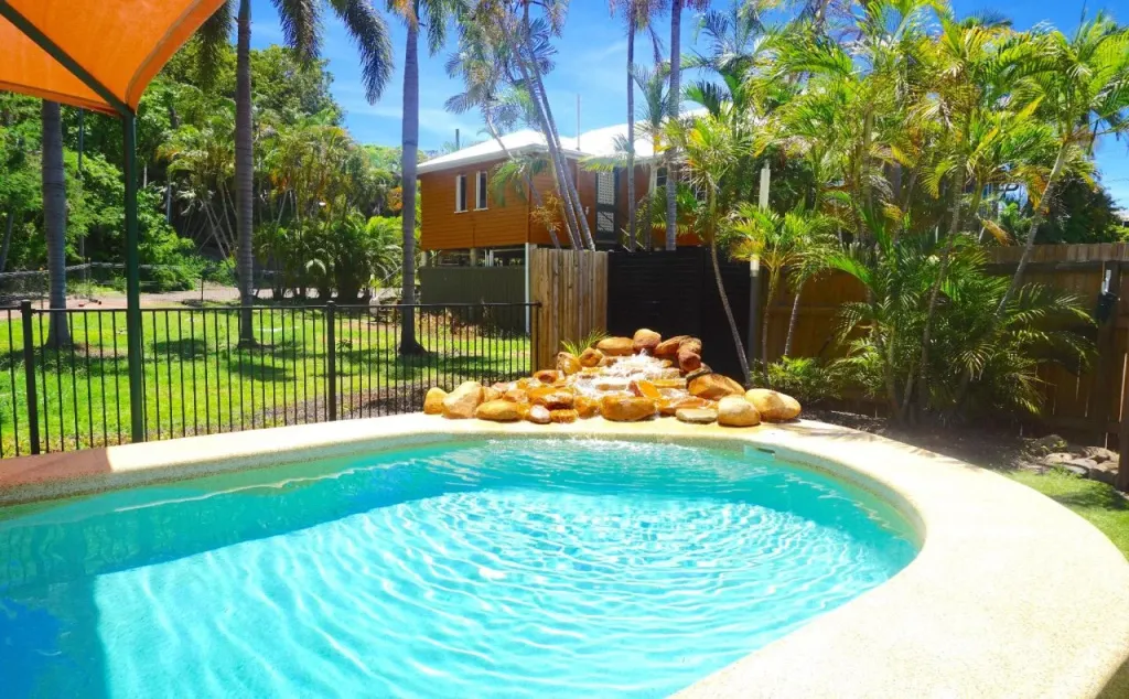 Une piscine turquoise bordée de rochers et de végétation luxuriante, avec un bâtiment orange en arrière-plan.