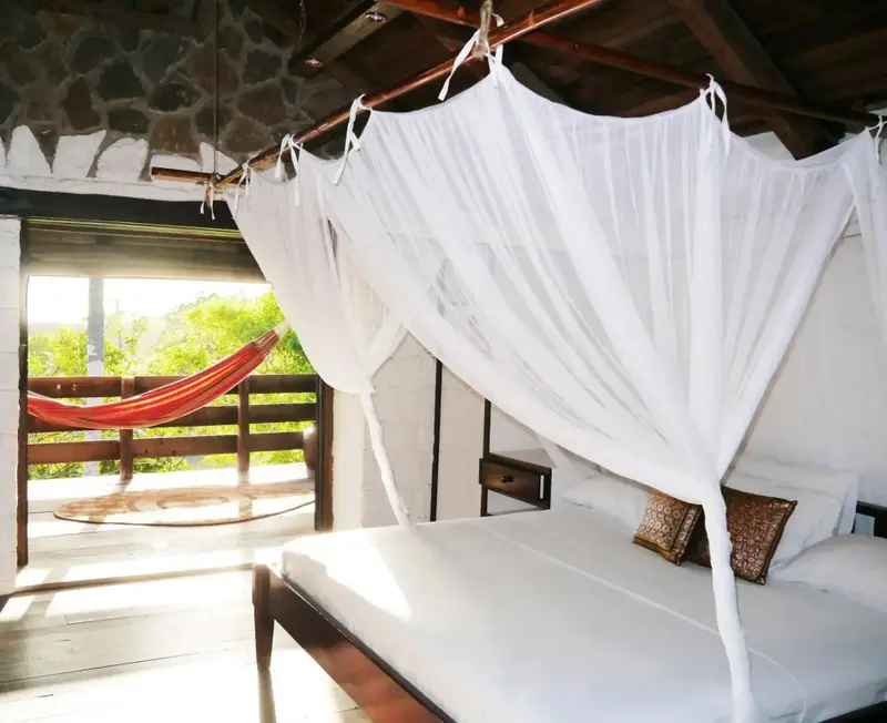 Une chambre lumineuse avec un lit à baldaquin et un hamac sur une terrasse.