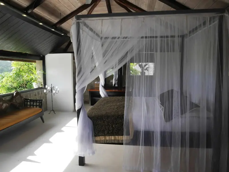 Une chambre lumineuse avec un lit à baldaquin et une vue sur la végétation.