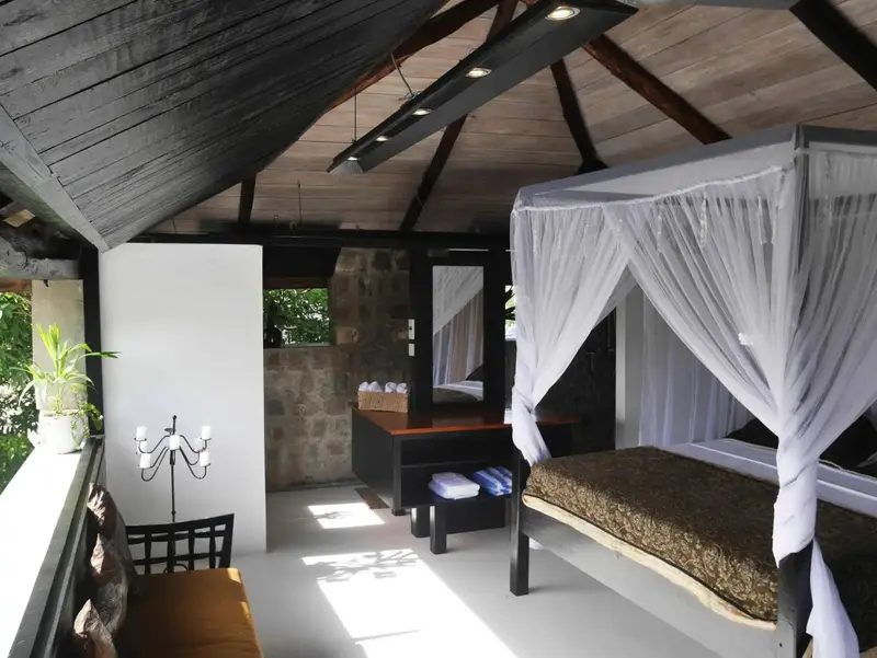 Une chambre lumineuse avec un lit à baldaquin et un espace salon attenant.