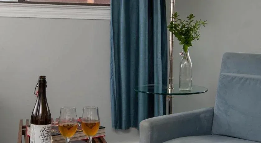 Une bouteille et deux verres de bière reposent sur une table basse près d'un fauteuil.