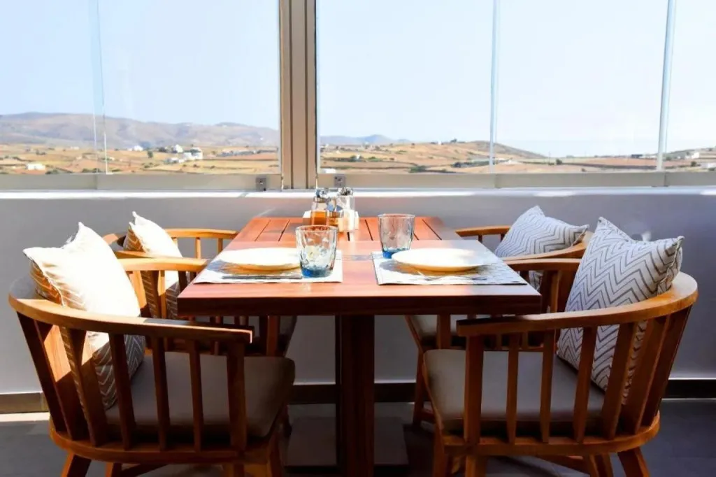 Une table est dressée devant une grande baie vitrée offrant une vue sur un paysage montagneux.