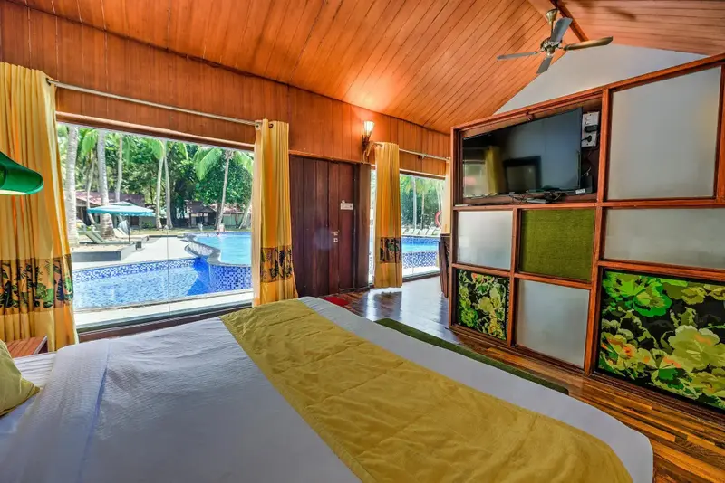 Une chambre lumineuse avec un grand lit donnant sur une piscine et une végétation luxuriante.