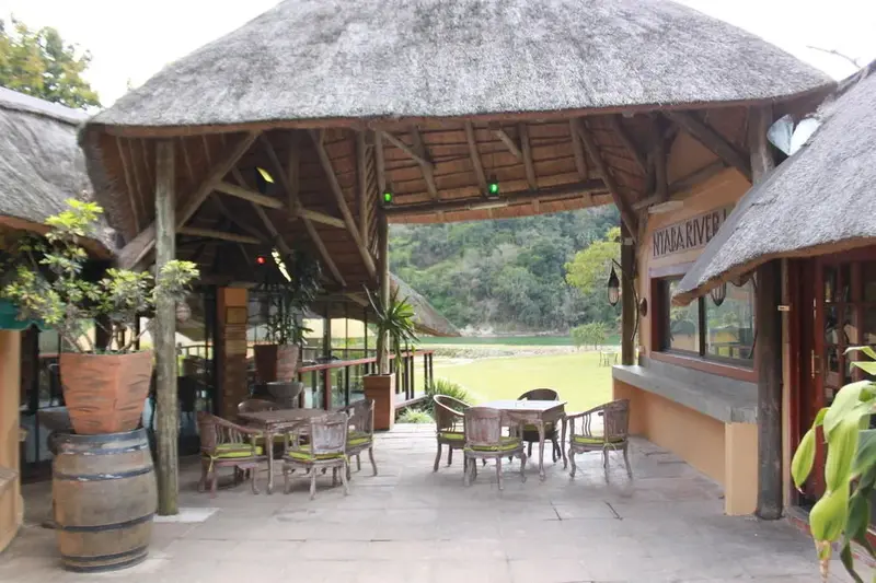 Terrasse ombragée avec tables et chaises donnant sur un paysage verdoyant.