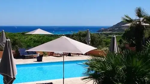 Une piscine bordée de transats sous des parasols, avec vue sur la mer.