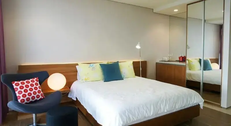 Une chambre lumineuse avec un grand lit et un fauteuil.