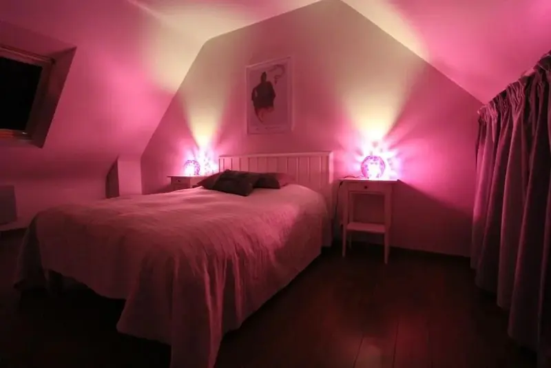 Une chambre aux murs inclinés est éclairée par des lampes de chevet roses.