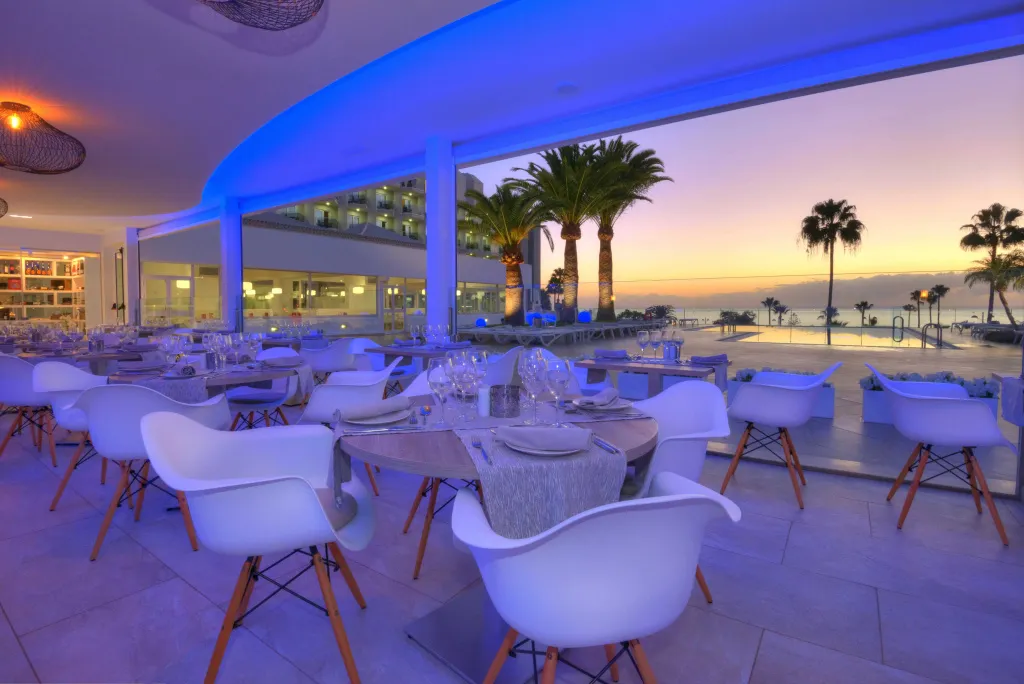 Tables dressées en terrasse avec vue sur la mer au coucher du soleil.