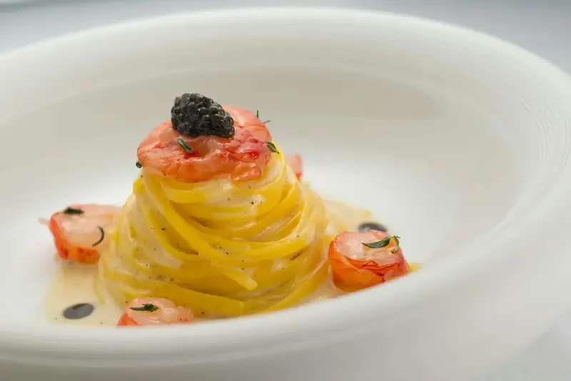 Un plat de pâtes aux crevettes et à la crème est présenté dans une assiette blanche.