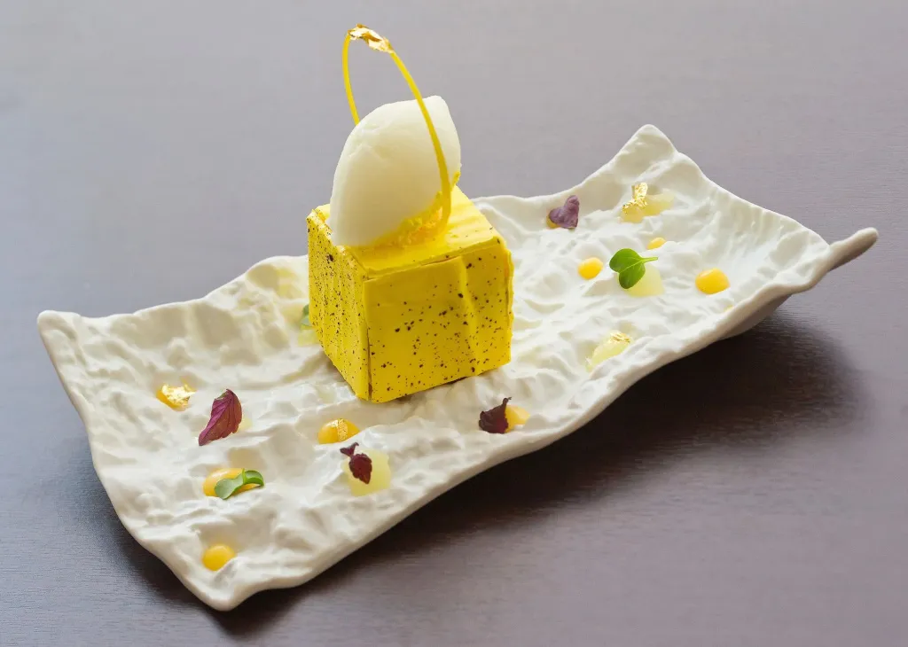 Un dessert jaune et blanc est présenté sur une assiette blanche texturée.