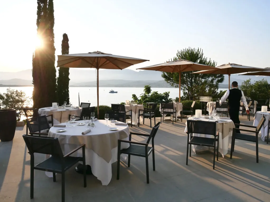 Tables dressées en terrasse avec vue sur la mer au coucher du soleil.