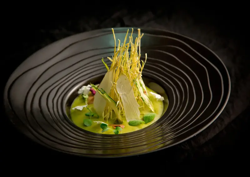 Présentation raffinée d'un plat gastronomique dans une assiette noire texturée.