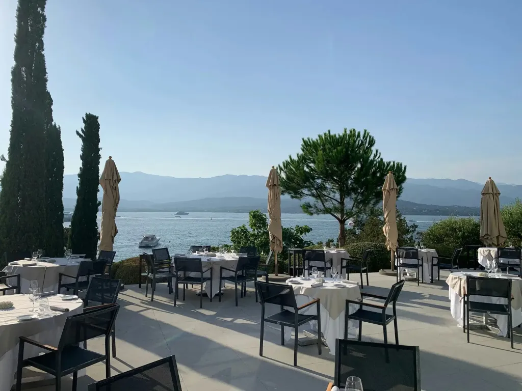 Terrasse de restaurant avec tables dressées face à la mer et aux montagnes.