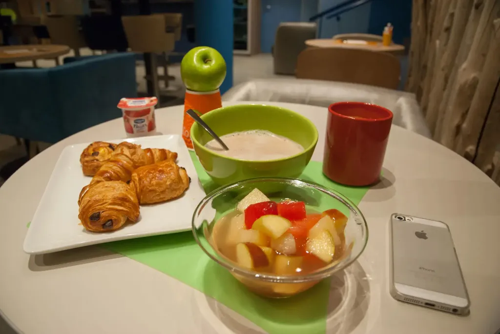 Une table ronde présente un petit déjeuner avec des viennoiseries, des fruits et des boissons.
