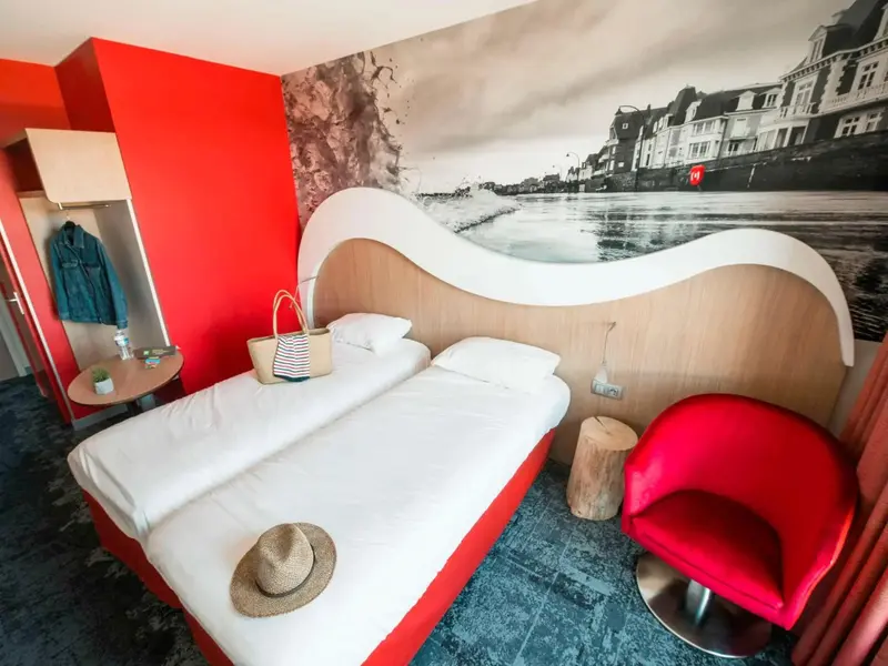 Une chambre lumineuse avec un lit blanc et un mur décoré d'une scène côtière.
