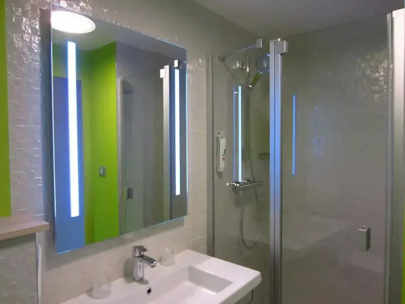 Une salle de bain moderne avec douche vitrée et grand miroir lumineux.