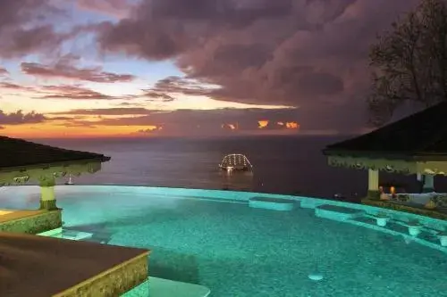 Une piscine à débordement surplombe la mer au coucher du soleil.