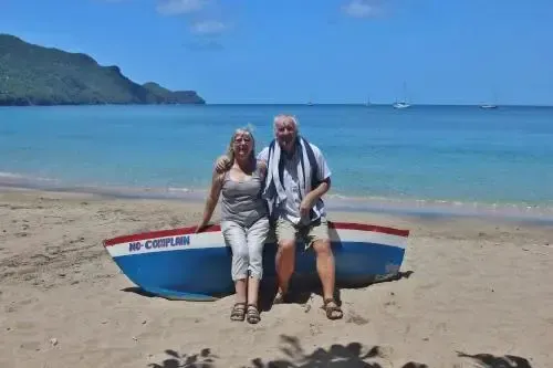 Un couple souriant pose devant un petit bateau échoué sur une plage de sable.