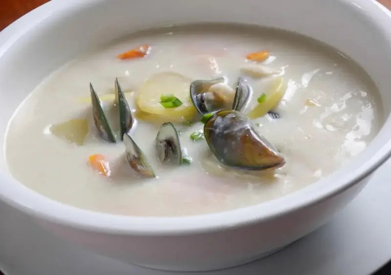 Une soupe de fruits de mer crémeuse est servie dans un bol blanc.