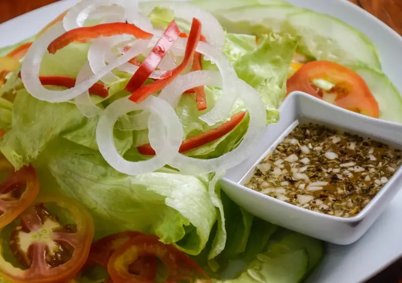 Une salade fraîche est présentée dans une assiette blanche avec une sauce à part.