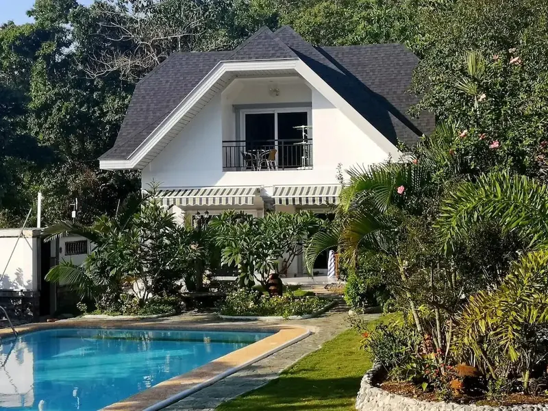 Une maison blanche avec un balcon fleuri surplombe une piscine turquoise.