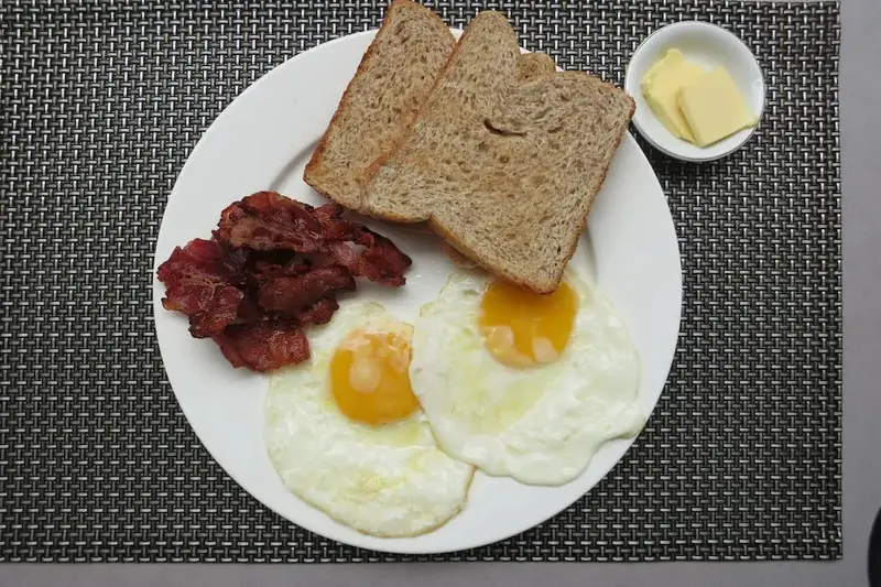 Petit déjeuner copieux avec œufs au plat, bacon et pain grillé.