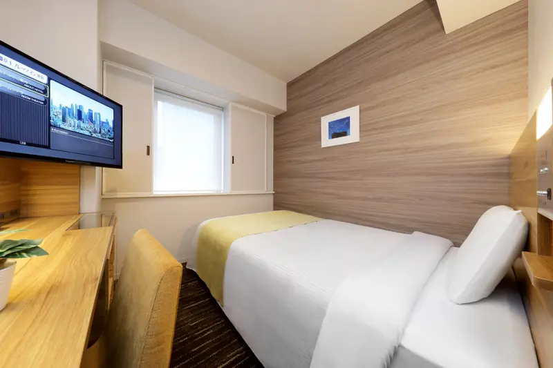 Une chambre d'hôtel lumineuse avec un lit simple et un bureau.
