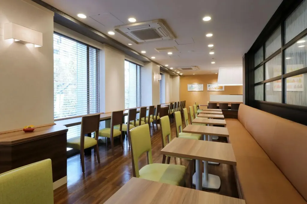 Une salle lumineuse avec des tables et des chaises alignées près de grandes fenêtres.