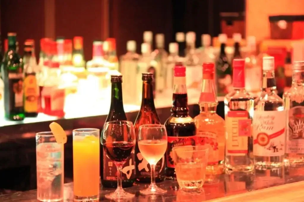 Un comptoir de bar présente une variété de bouteilles et de verres colorés.